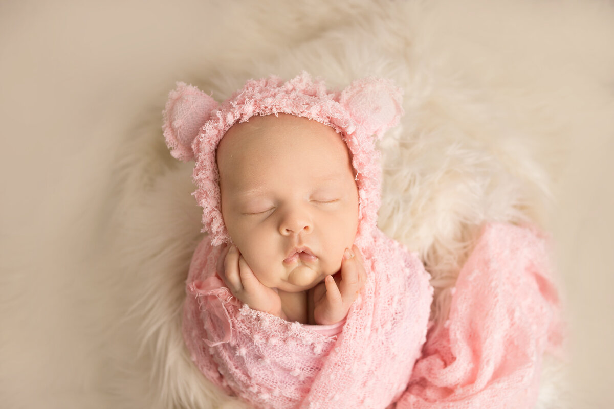 Newborn baby wearing bear bonnet wrapped in pink wrap during newborn photoshoot in Franklin Tennessee photography studio