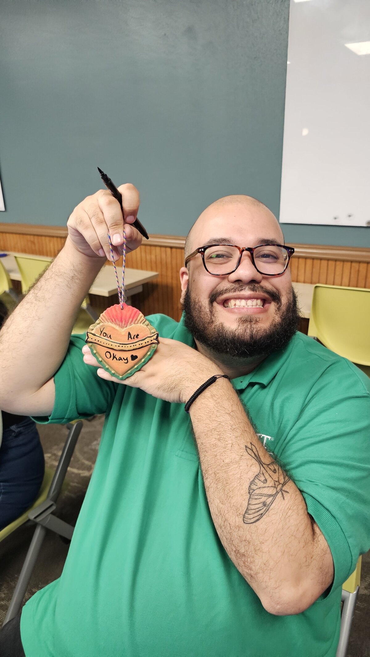 The vibrant artistry of a male workshop participant as he proudly displays his colorful heart graphic piece at Soleil Vida Studio. Dressed in a neon green t-shirt and sporting black reading glasses, his individual flair shines through