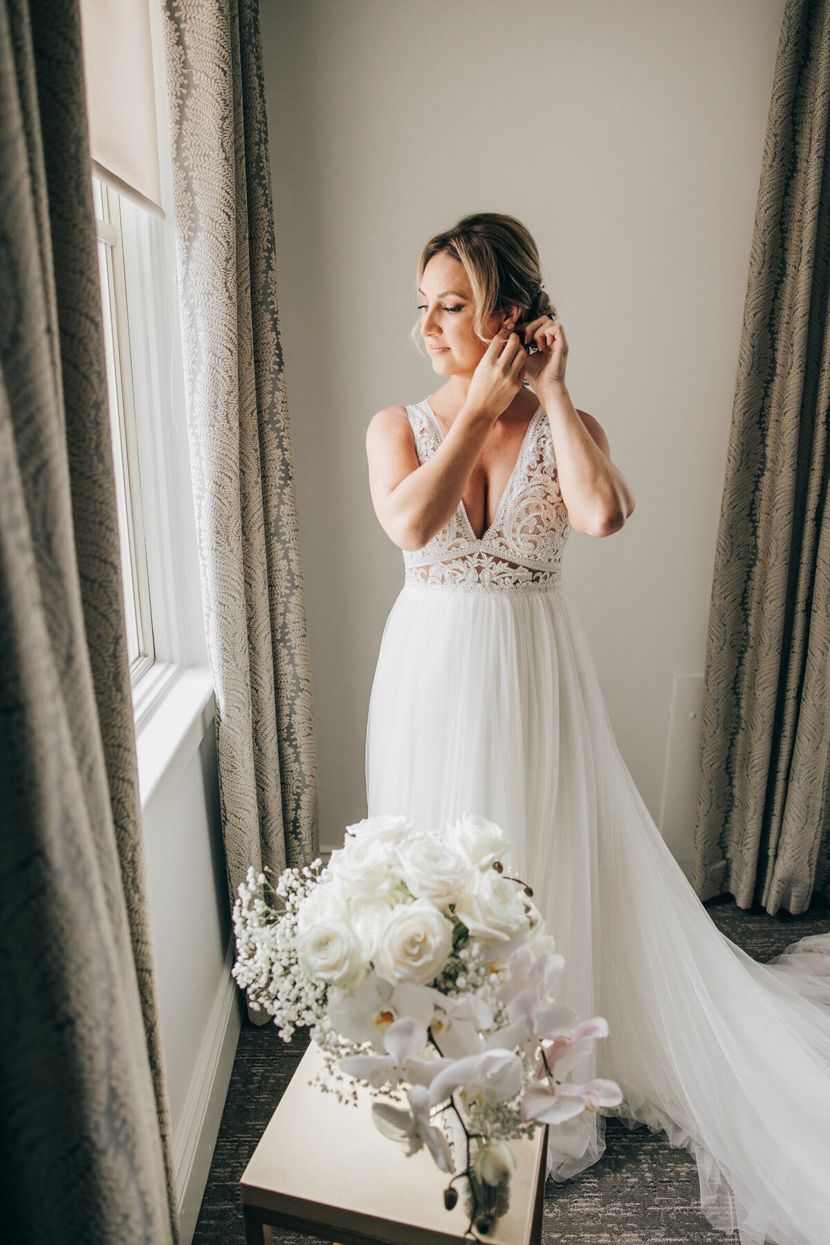 A bride putting on earrings while looking out a window