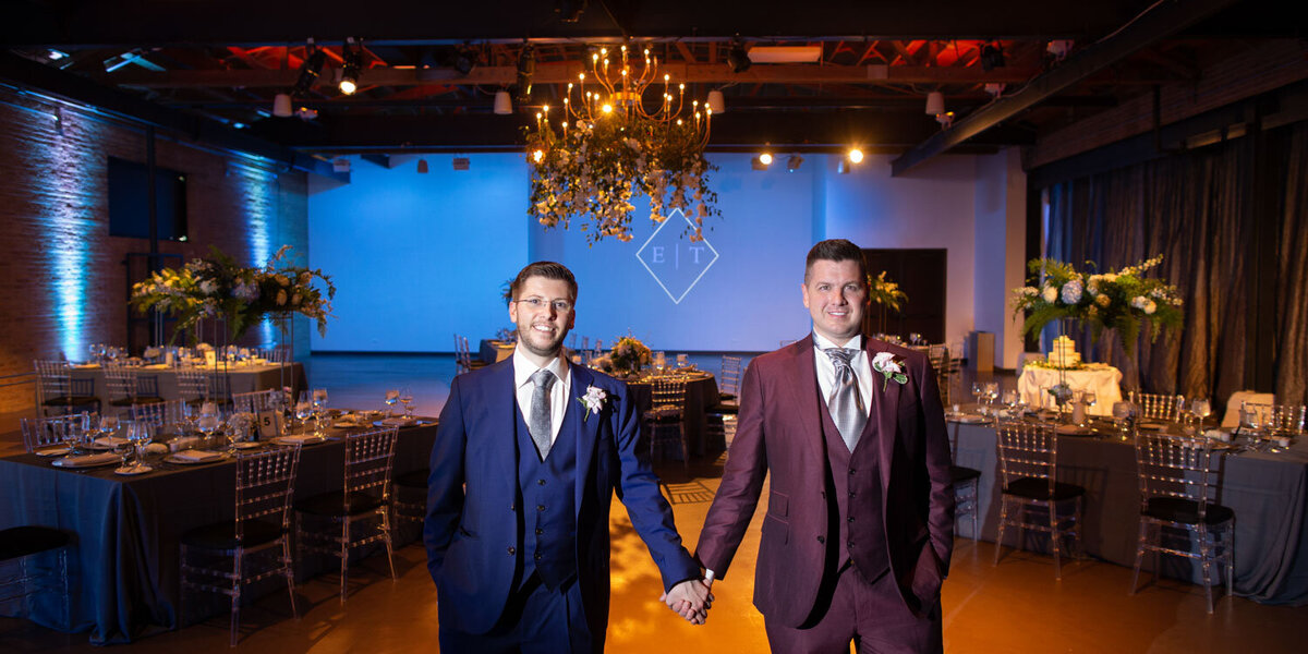 Two men in suits are holding hands in a room.