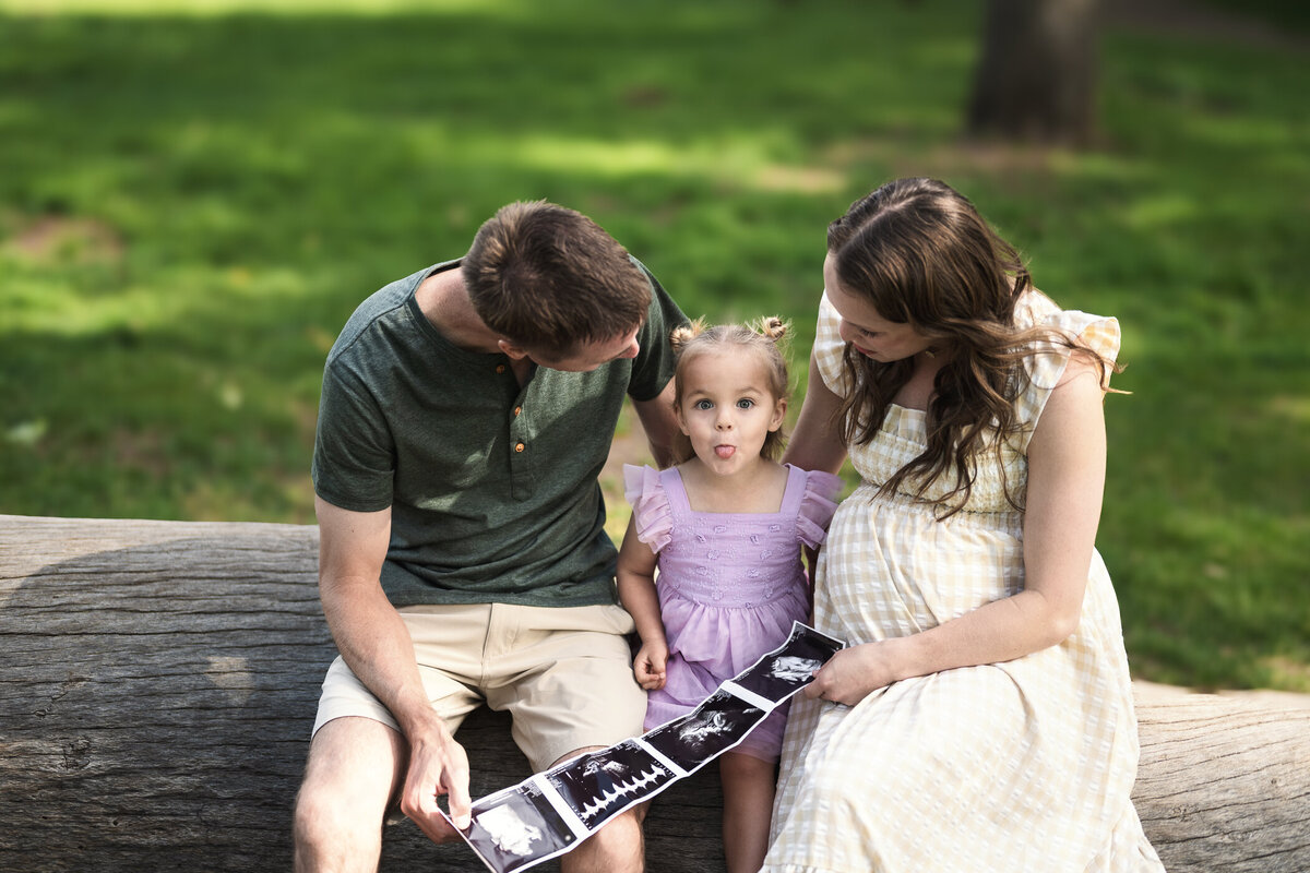 Image of a little girl sticking her tongue out sitting between mom & dad holding a sonogram.
