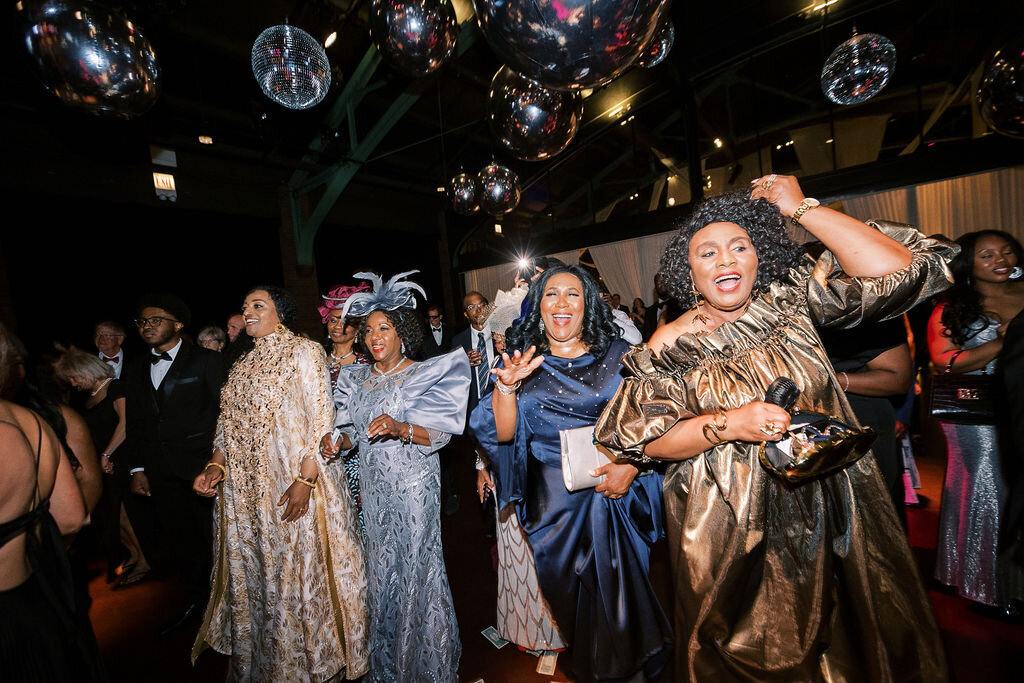 A group of elegantly dressed women in shimmering gold and blue gowns dancing and celebrating under mirrored disco balls.