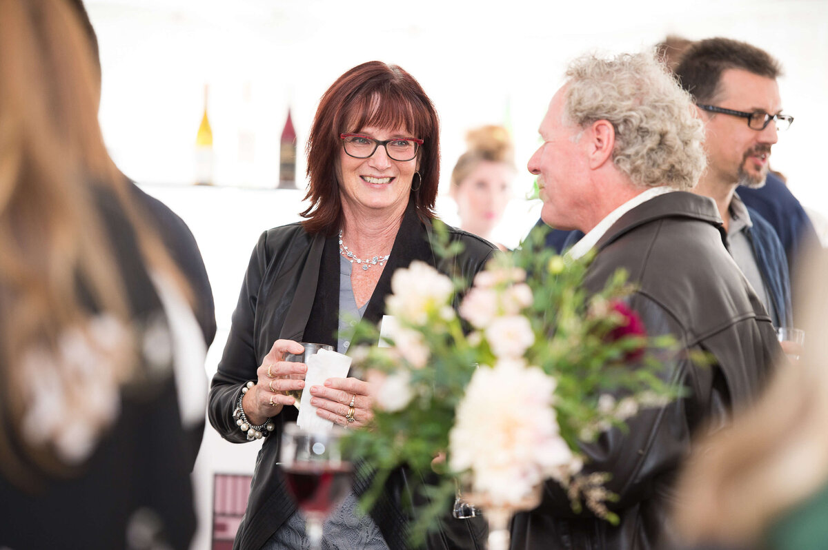 a photo of woman holding a drink and smiling at a guest at a corporate anniversary celebration.  Captured by Ottawa Event Photographer JEMMAN Photography COMMERCIAL