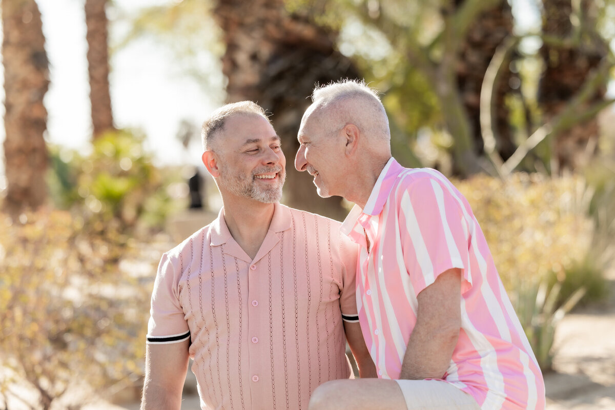 Older LGBTQ+ couple embracing in soft natural light, wearing coordinating pastels during a romantic Palm Springs moment.