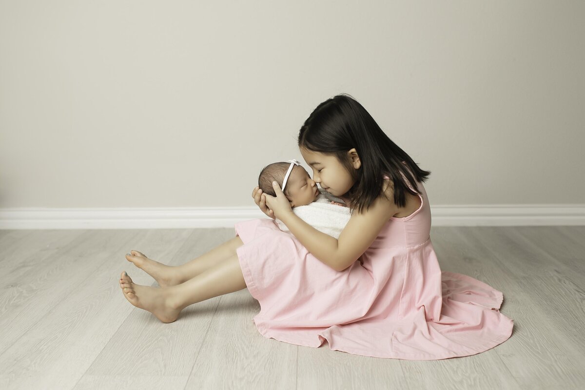Loving big sister gently holding her newborn baby brother and sweetly giving him kisses, capturing a tender and heartwarming sibling momen