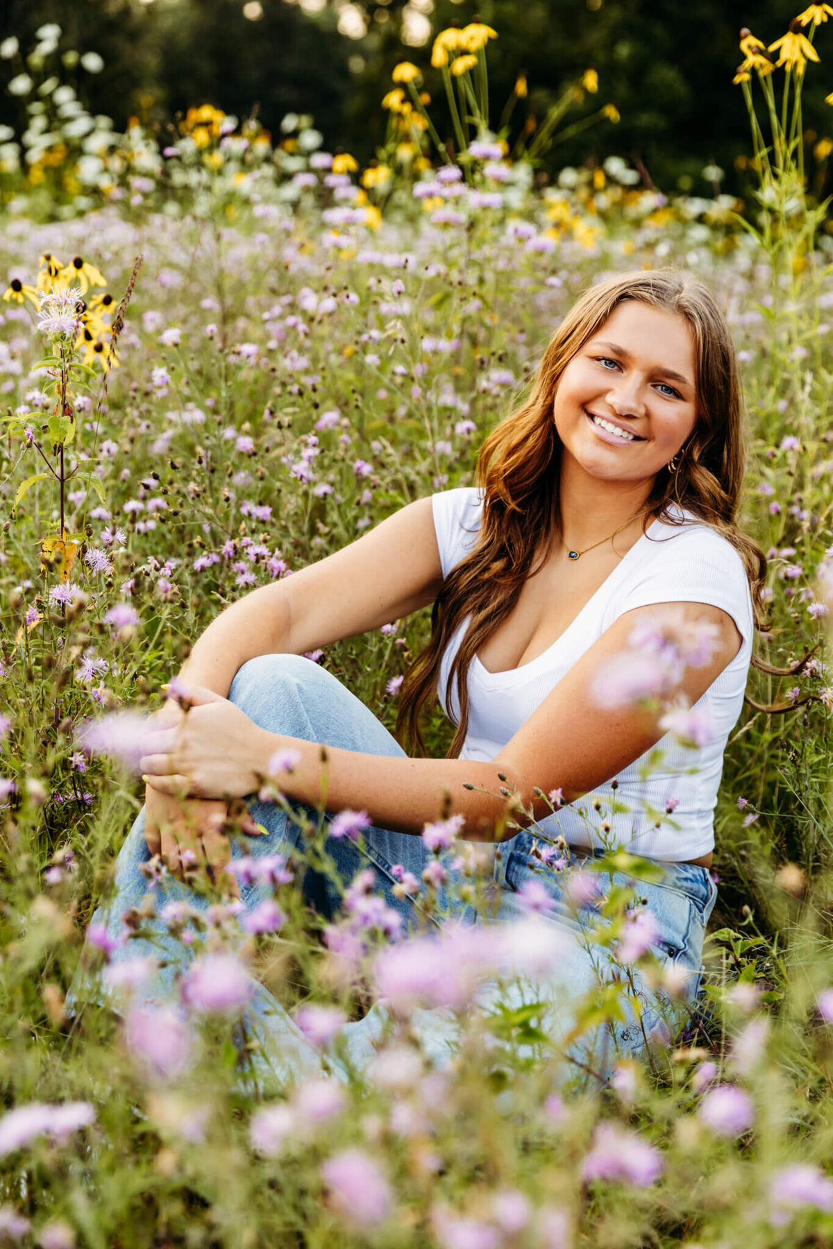 beautiful teenage girl from Appleton sitting in a sea of wildflowers and smiling as she enjoys her senior photo session.