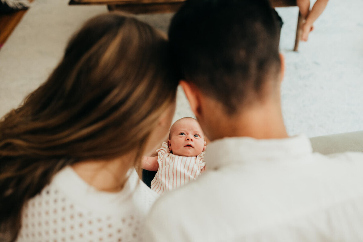 A mother and father lean their heads together as they look at their newborn daughter, their baby looks right up at them during their photoshoot with Boston Newborn Photographer, Allison Wolf