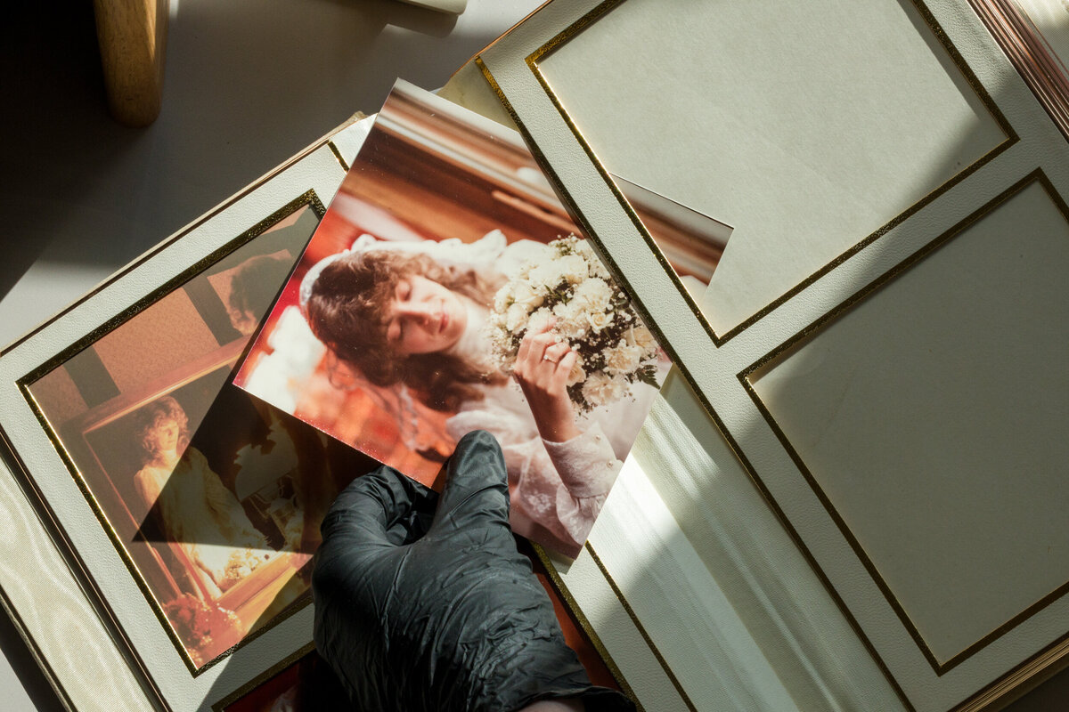 Black-gloved hands carefully removing a wedding photo from an old album during restoration.