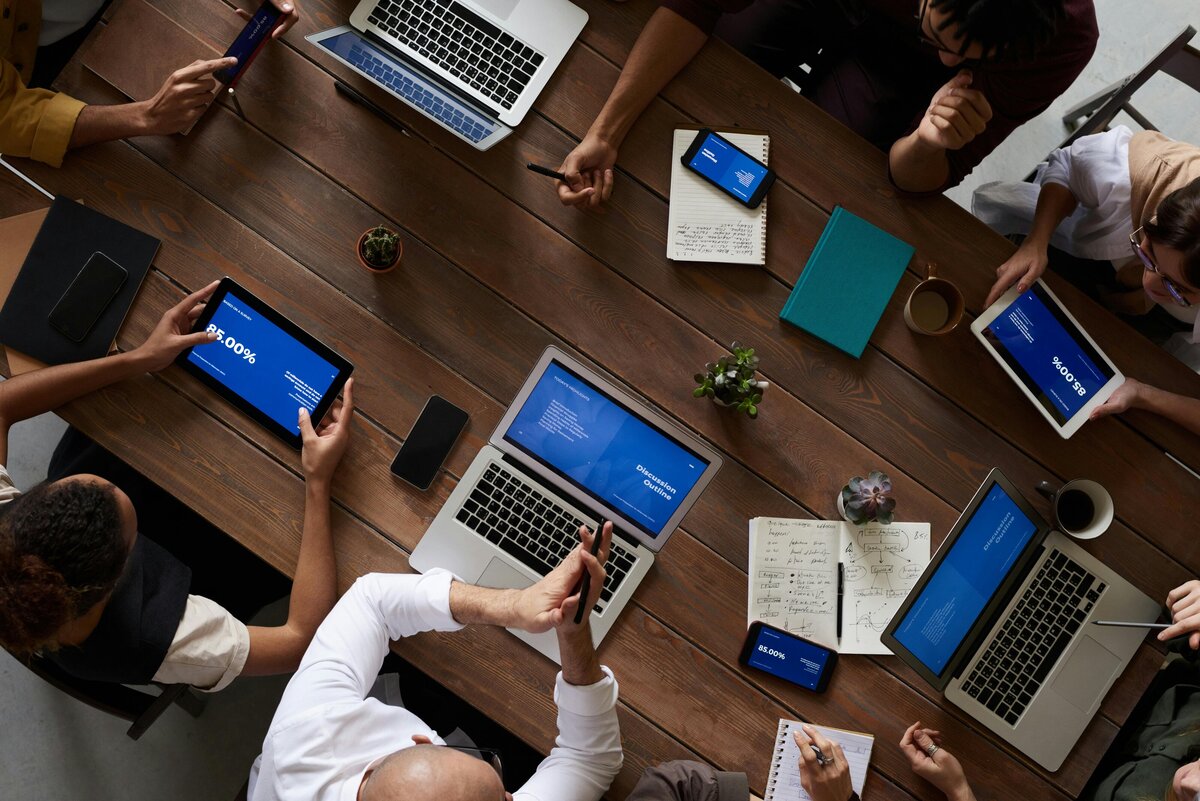 Overhead view of numerous coworkers sitting around a large table with tablets and computers