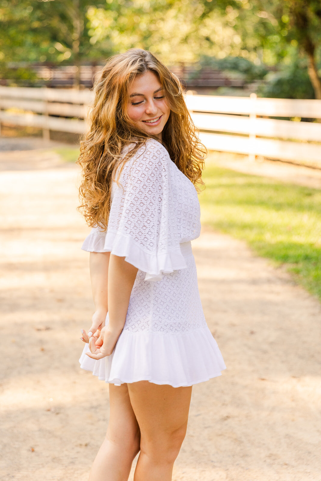 senior girl standing sideway and looking down her shoulder hands in the back during portrait session in Atlanta park
