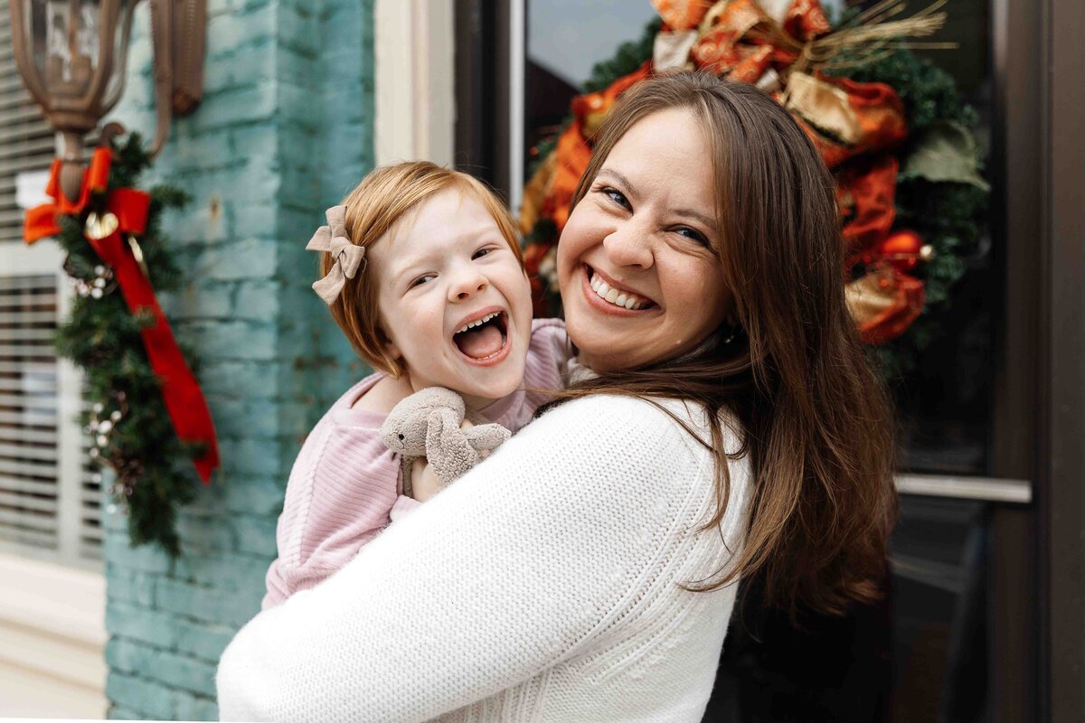 Mother holding daughter and both are laughing and smiling at the camera
