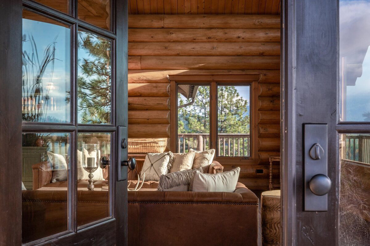 Rustic living room with wooden beams and large windows overlooking a forest, Photo by Moore Creative.
