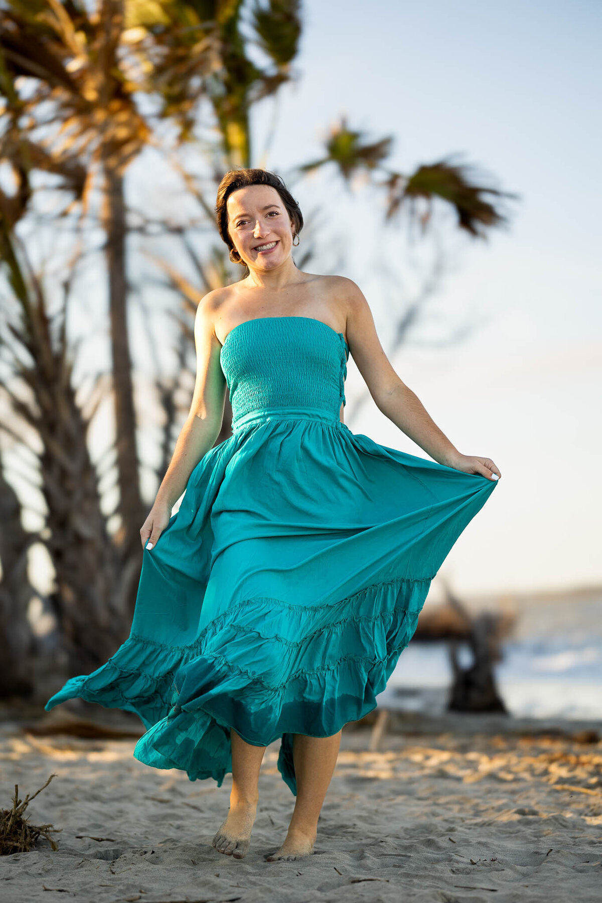 A senior girl in a teal boho maxi dress twirls outdoors, with the wind catching her dress perfectly, creating a dramatic and whimsical portrait.