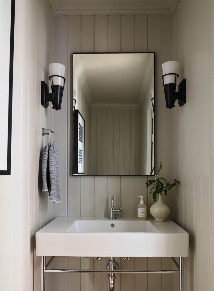 Discover the new powder room off the kitchen in a historic Hingham home, featuring light grey shiplap walls, a console sink with chrome legs, and a ceramic basin.