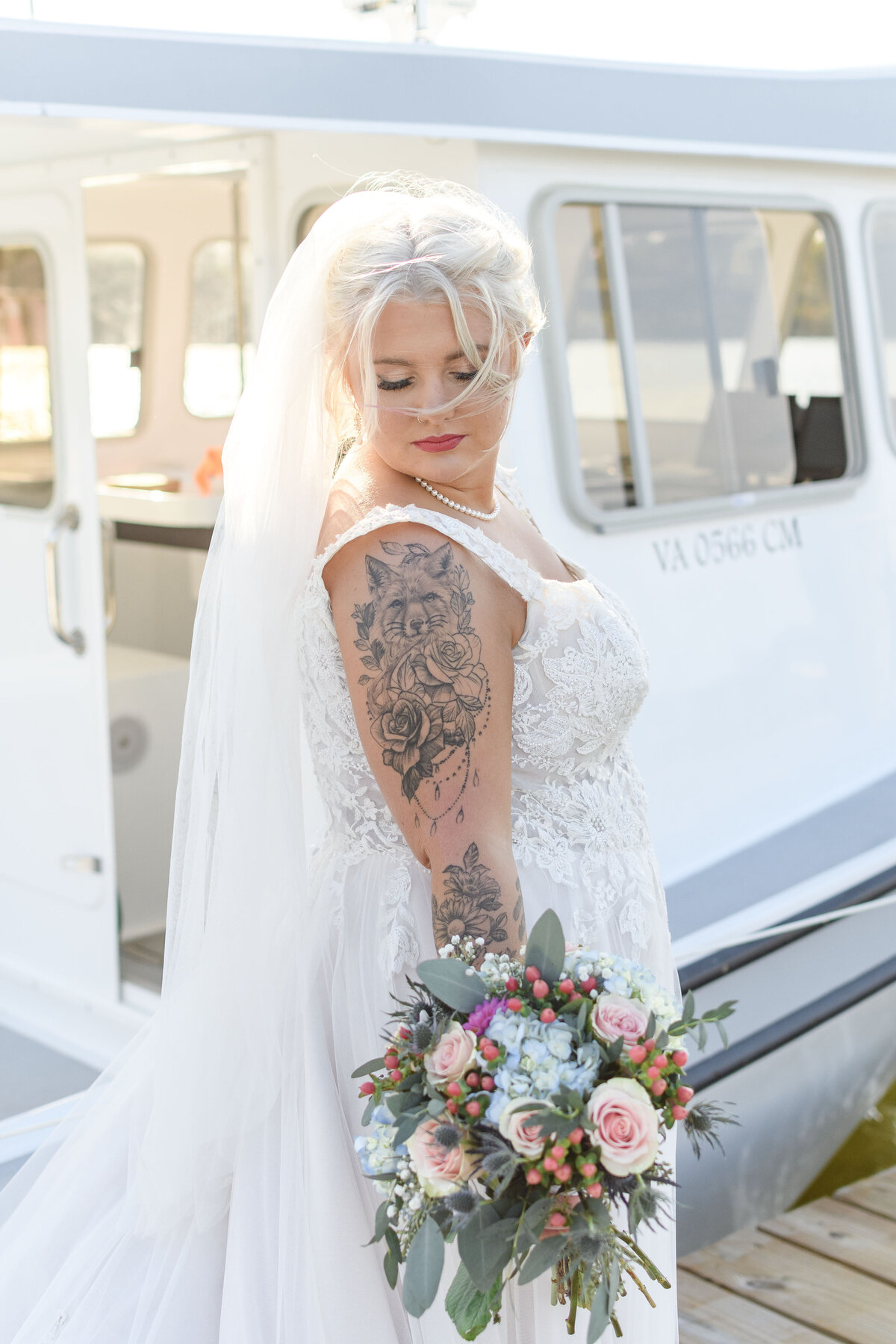Bride looking at her bouquet with her father's boat in the background