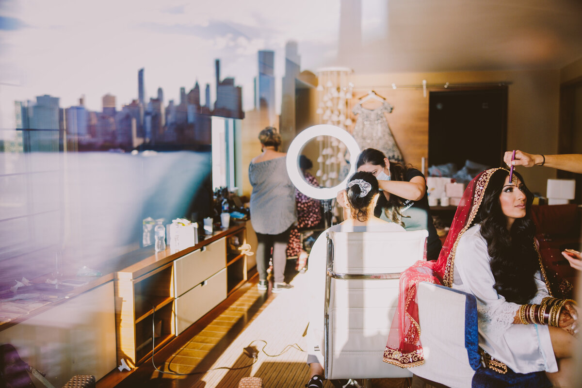 Photo taken through the glass of the indian bride getting ready for the wedding with the nyc skyline in the reflection