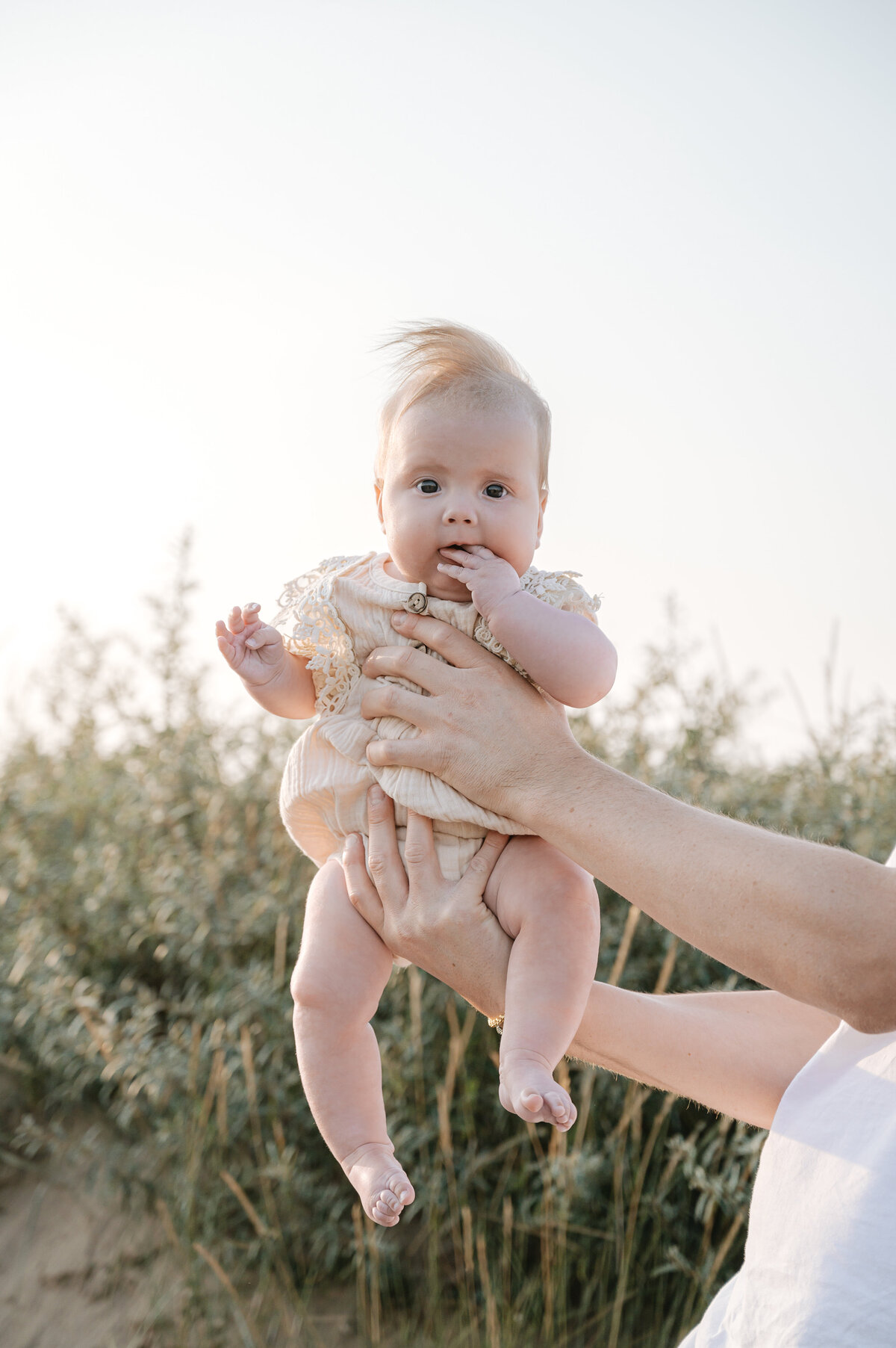 Outdoor baby photography of a father holding his daughter in the air in a field