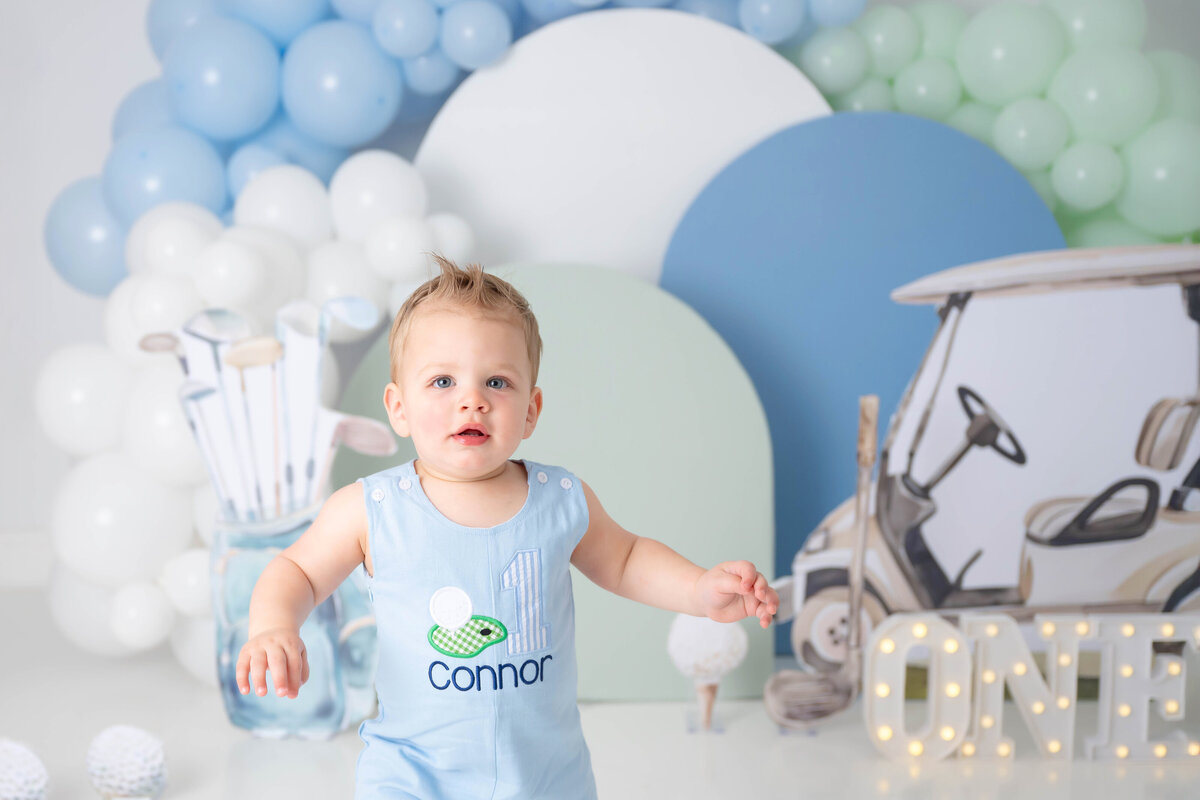 Close-up of a toddler wearing a light blue romper with a golf ball and number detail on it.