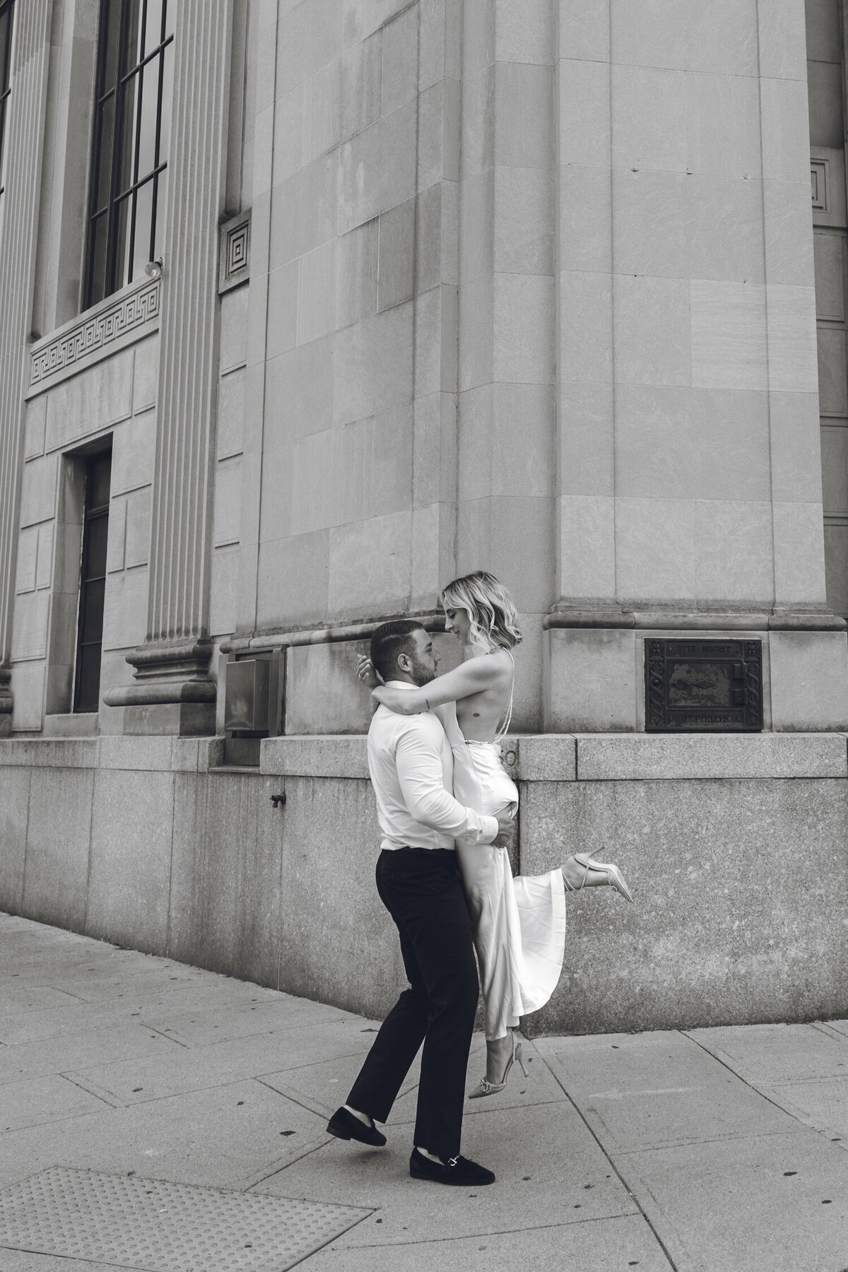 Groom lifting bride in a dramatic dip on city sidewalk.