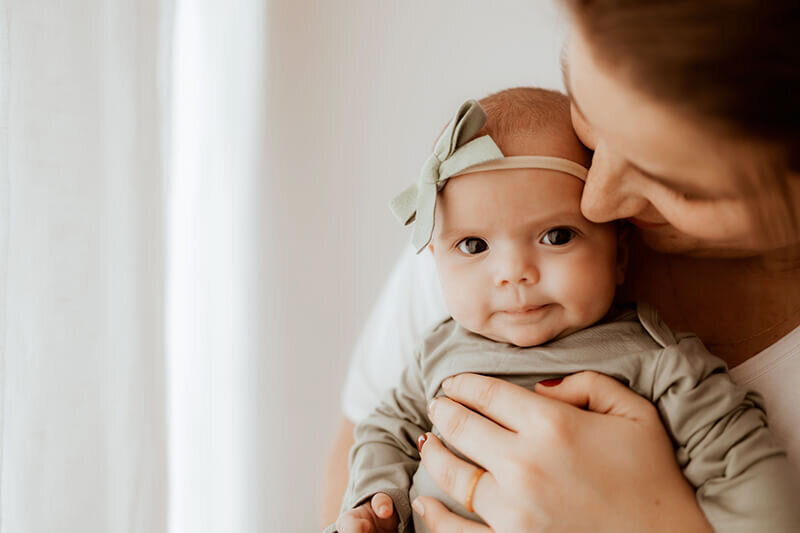 Mom kissing newborn baby girl's cheek during newborn session in studio