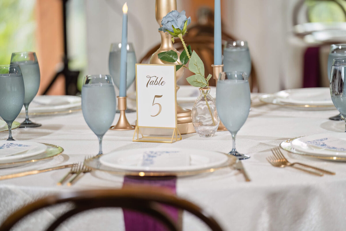Elegant wedding reception table with a modern gold table number and fine glassware.