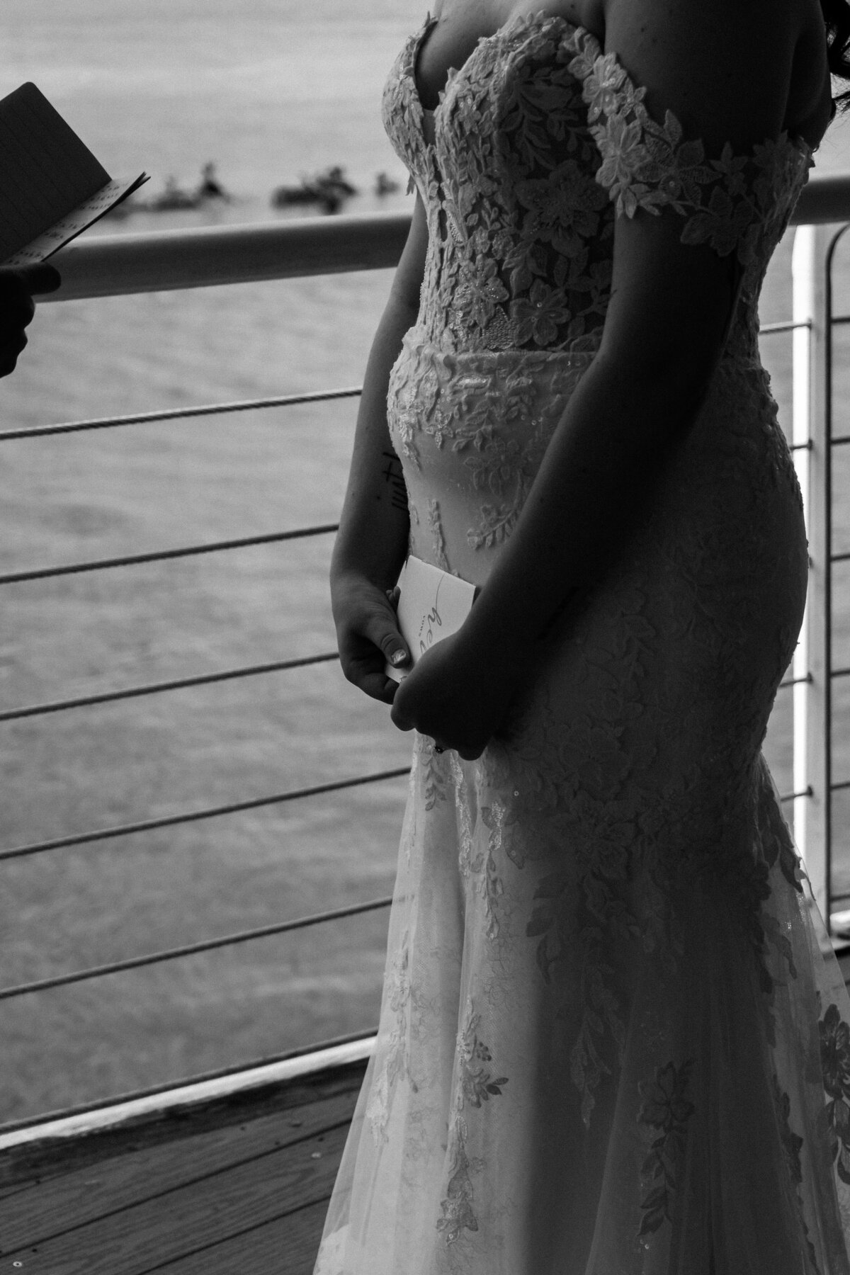 A close-up, black and white portrait of a bride in her wedding gown holding her vows, standing by the waterfront railing at the Lesner Inn in Virginia Beach, captured by Quinn Photography LLC.