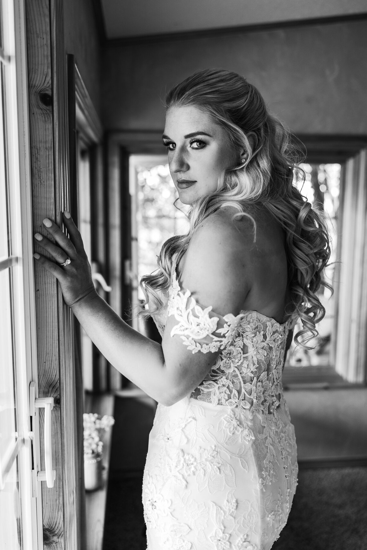 Black and white portrait of a serious bride getting ready for her wedding day by a window, reflecting on the moment