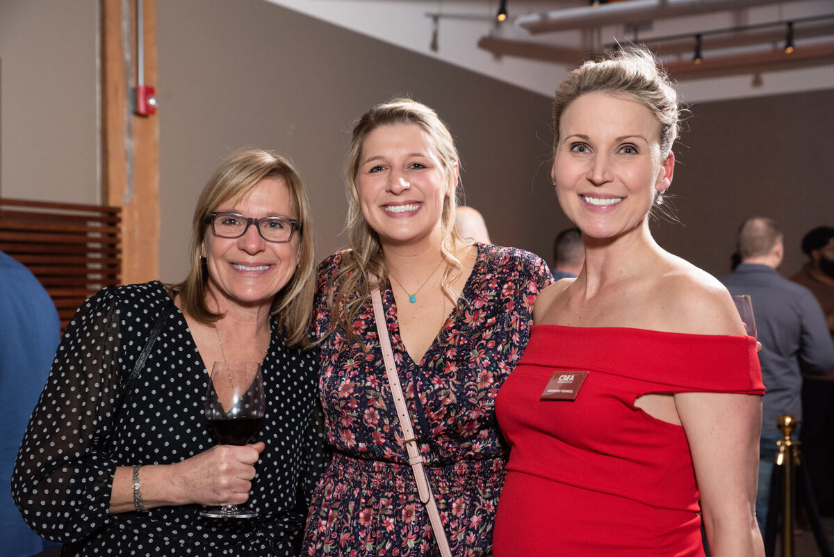 Three women smiling at a party with drinks in hand