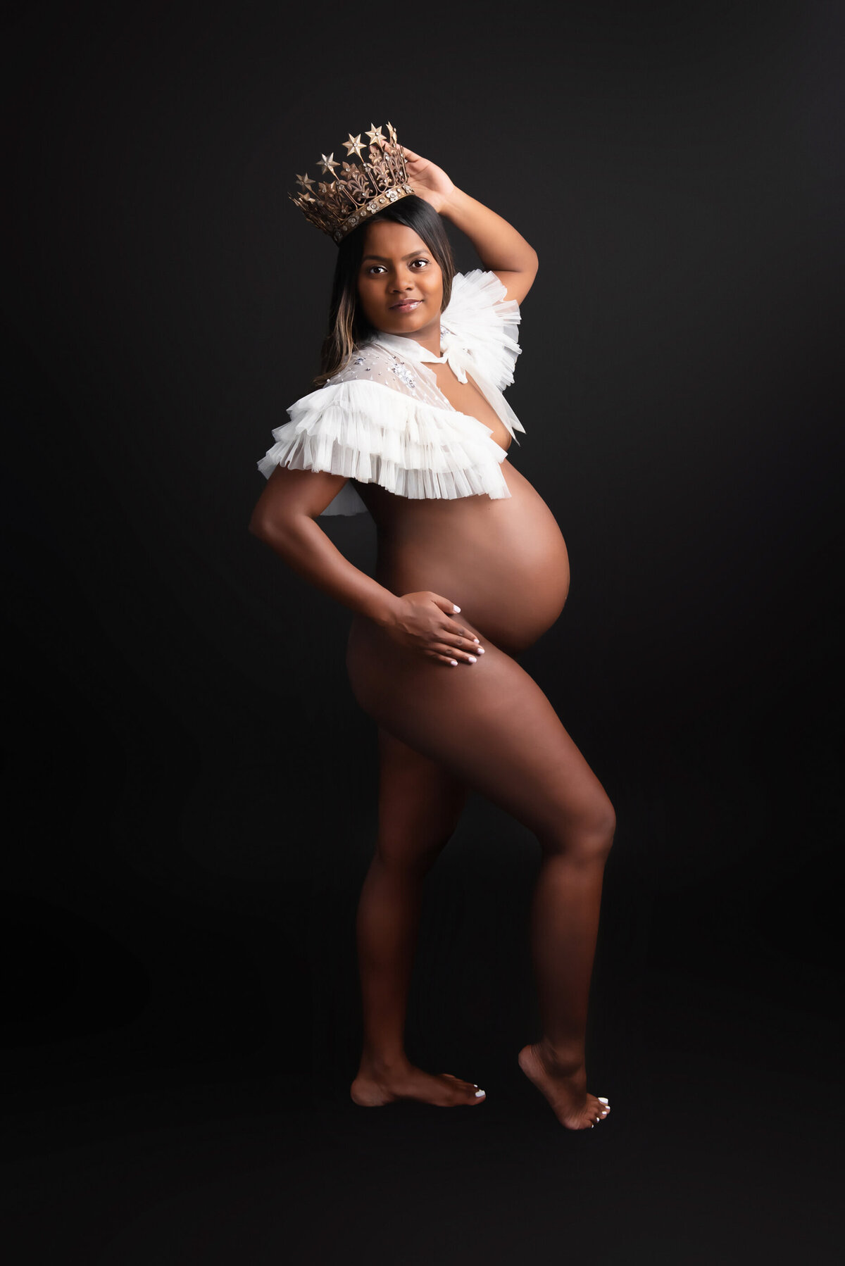African American woman wearing a white shall and crown for her studio maternity photography session
