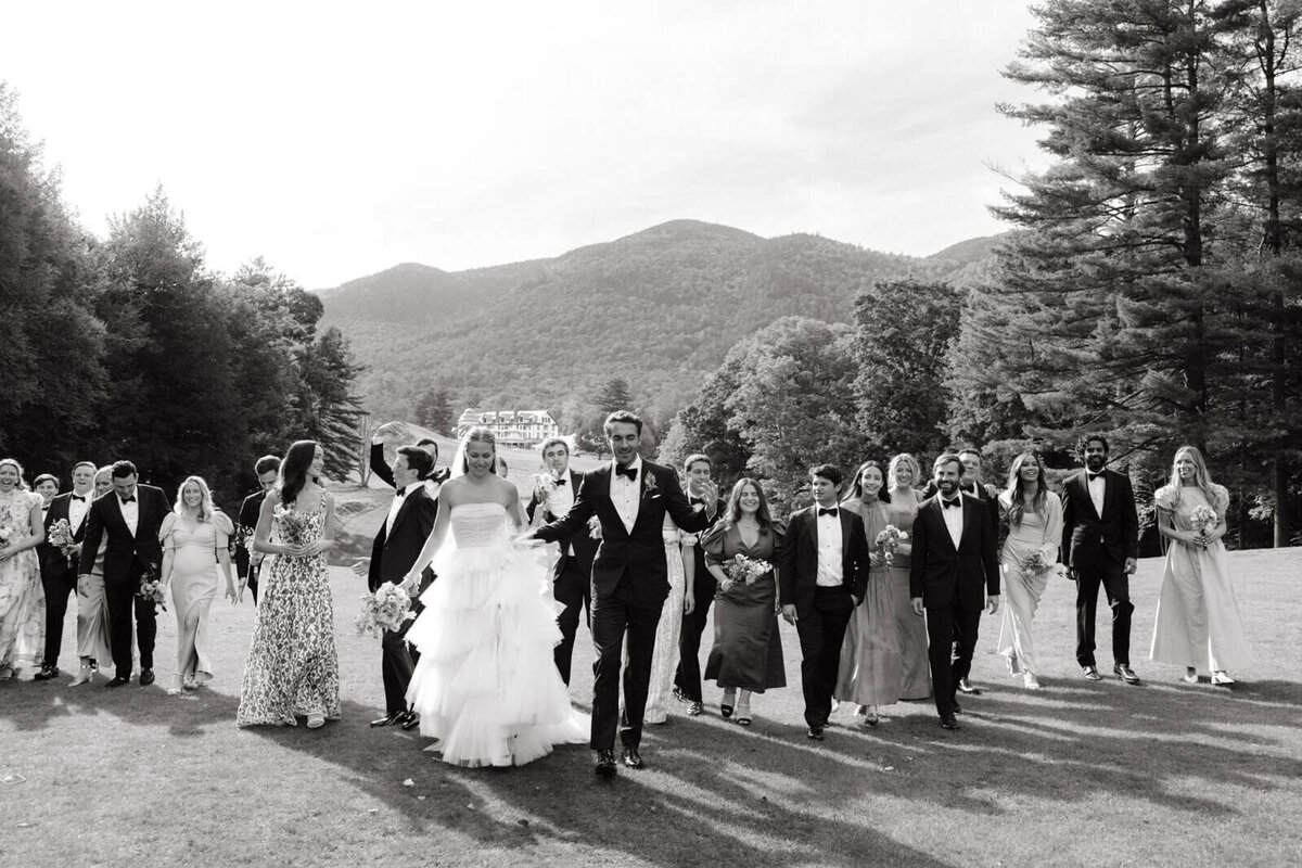 The bride and groom, bridesmaids and groomsmen are at The Ausable Club golf course, with trees and mountains in the background.