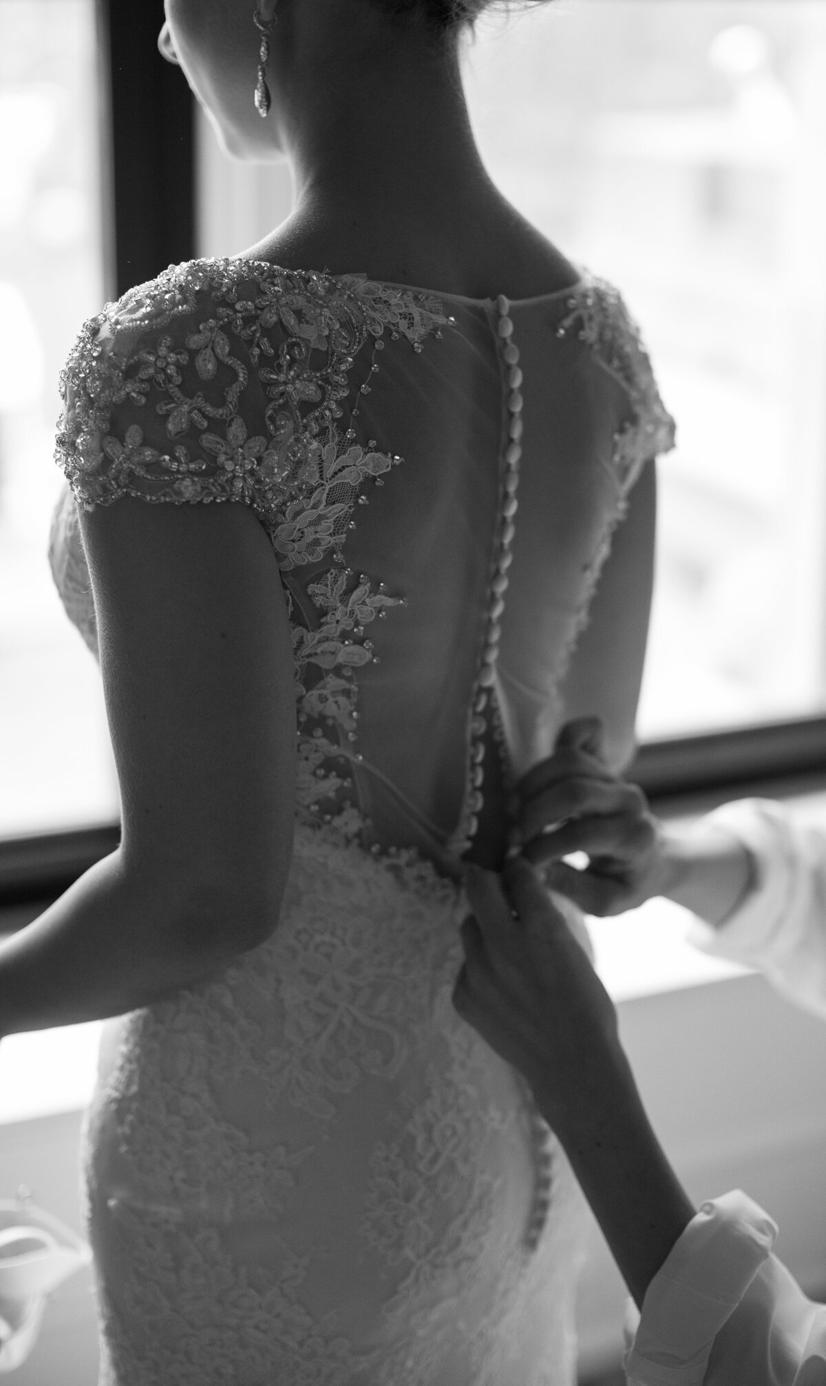 Bridesmaids hands button up brides elaborate wedding dress back.