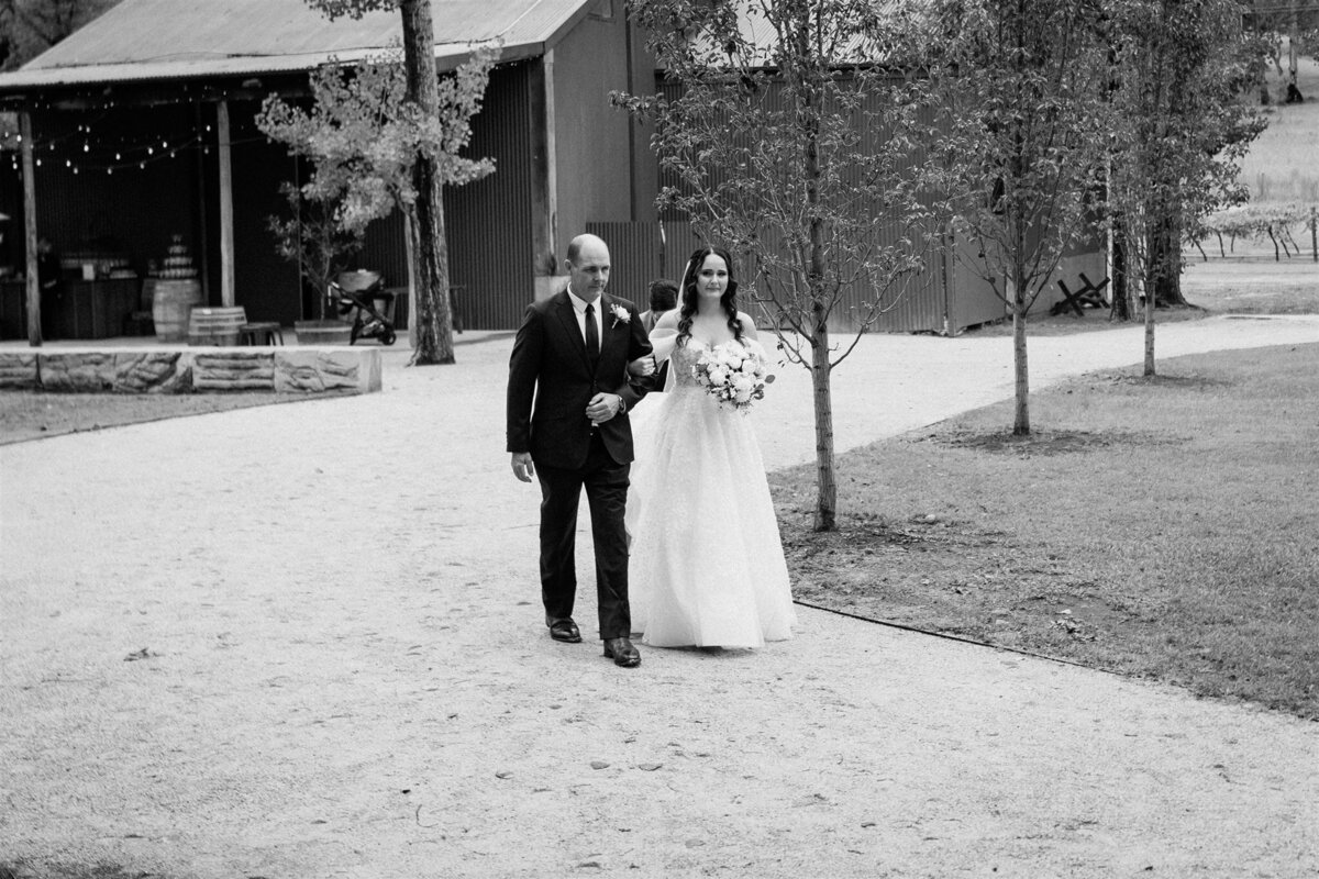 A radiant bride, her hand gently clasped in her father's, glides down the aisle, her eyes gleaming with anticipation and joy.