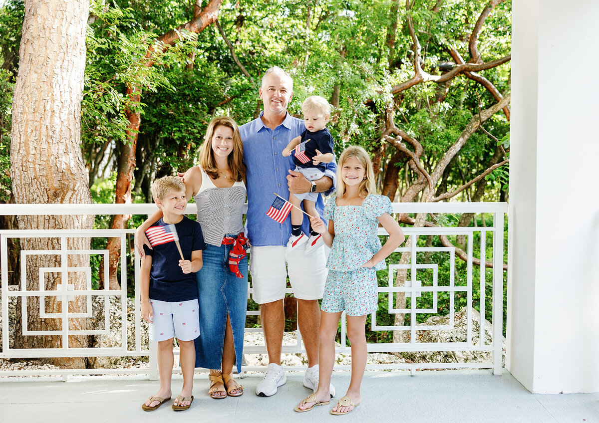 A smiling family poses with small American flags against a lush green backdrop during a Florida Keys family session.