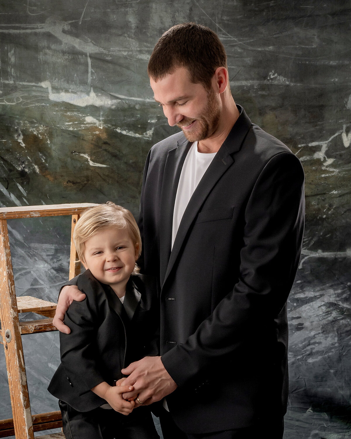Dad looking down and hugging his laughing son standing on a ladder
