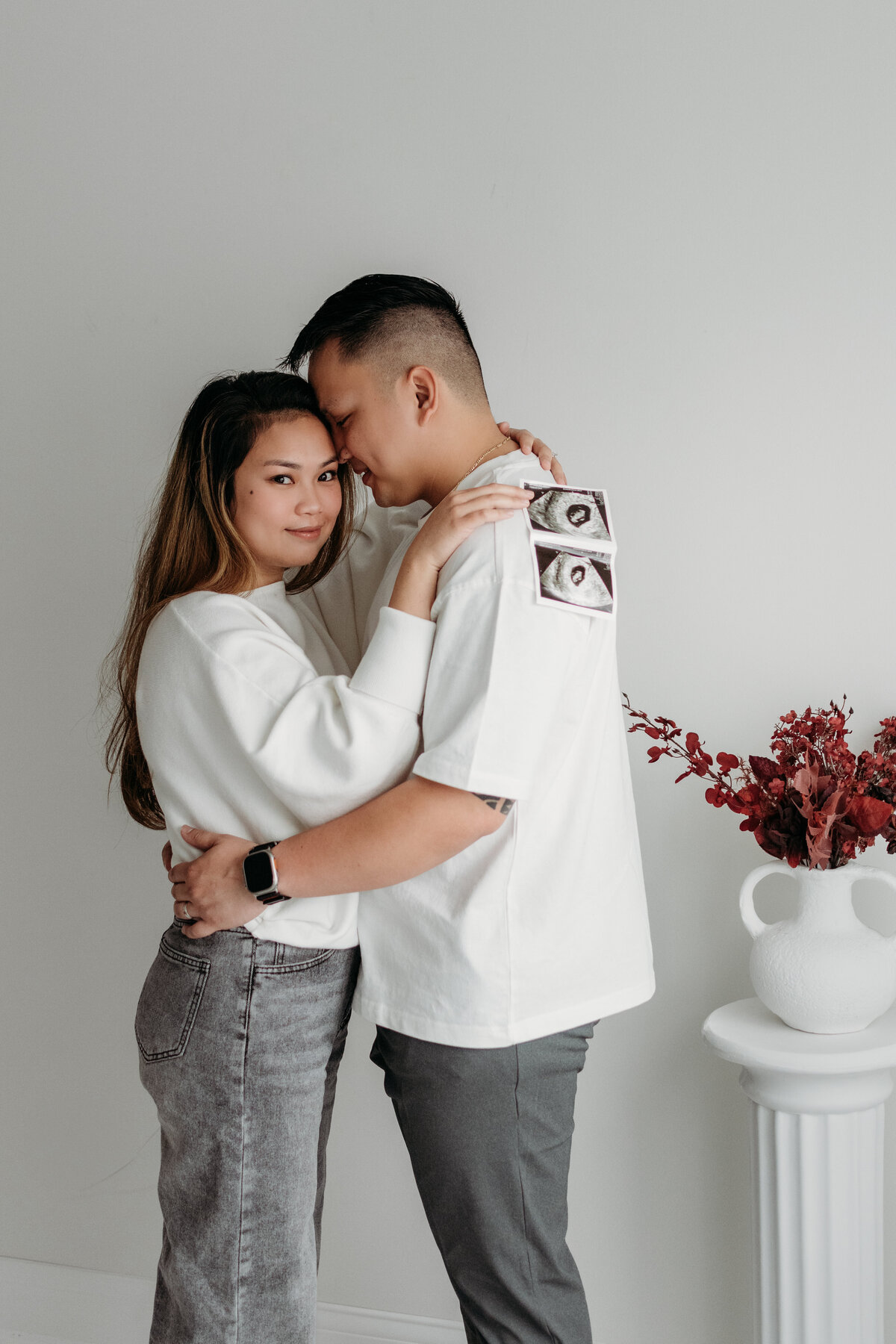 A sweet embrace between mom+dad to be during a pregnancy announcement photoshoot in a light filled studio in bartlett, il