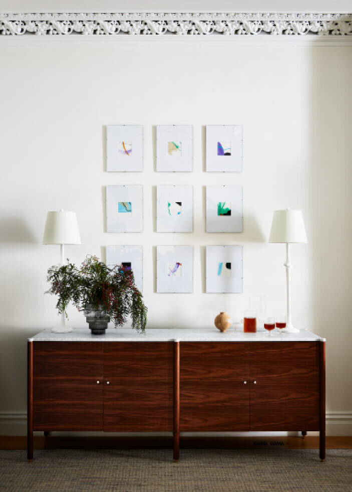 Boston Area Interior Designers designed a modern dining room with a walnut console, marble counter, plaster white lamps, simple art, and original plaster ceiling molding.