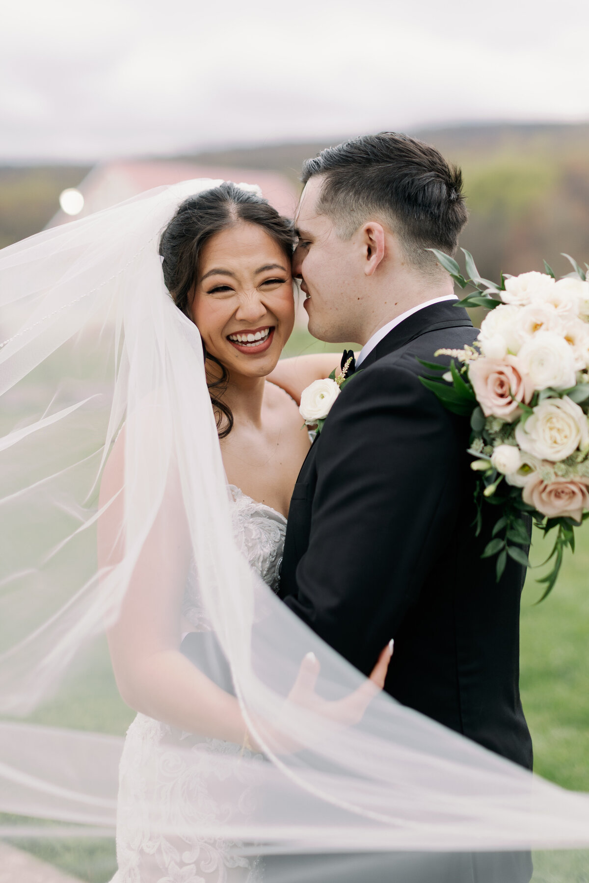 Bride and groom embracing beneath flowing veil with bouquet by Flowers by Wendy Carol at Springfield Manor.