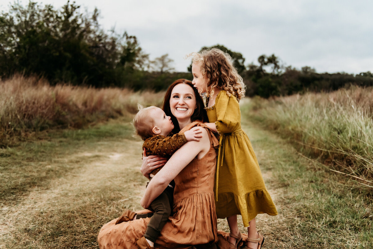 Family Photographer, Little girl snuggling mom's back, while mom is holding baby boy.