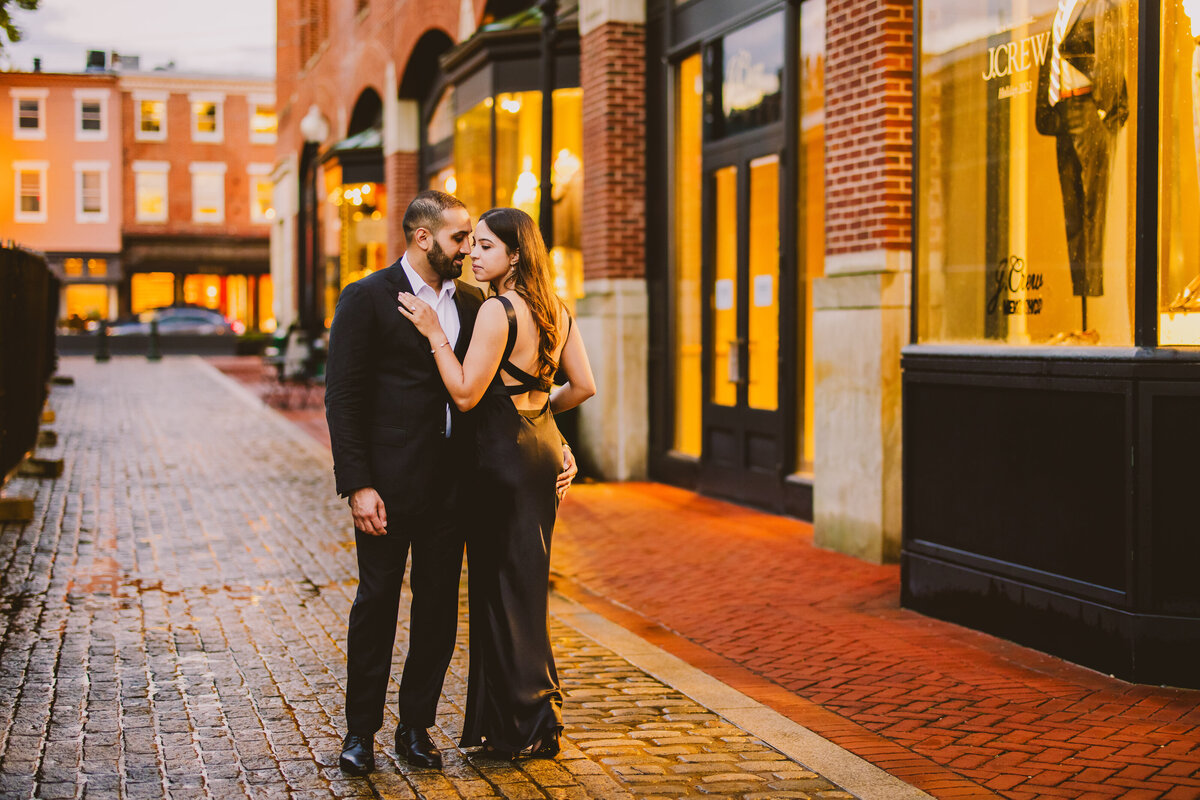 An engaged couple in black formal outfits share a moment in in the evening on brick road in georgetown dc