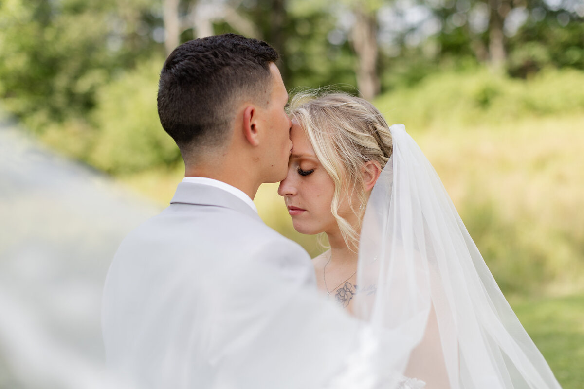 Bride and groom facing each other while the groom is kissing the bride on her forehead