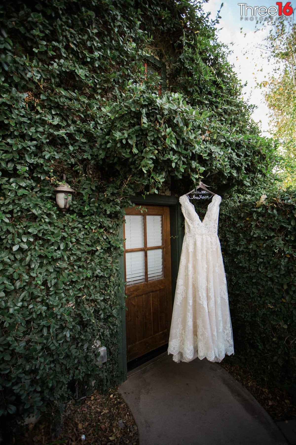 Bride's wedding dress hangs on display in front of a cottage with ivy covered wall and a door