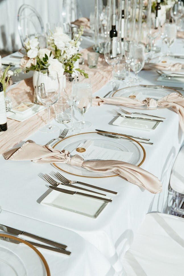 This image captures beautifully arranged place settings and centerpieces on long tables, showcasing an elegant wedding setup. Each setting features refined details, including stylish tableware and stunning floral arrangements, perfect for enhancing any event. Ideal for couples planning their Ottawa weddings, this photo illustrates our expertise in creating memorable dining experiences with a focus on modern design elements.