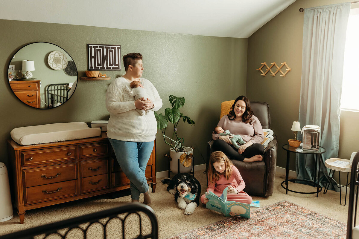 Two moms hold twin babies while 6 year old daughter reads to their dog in Fort Collins, CO