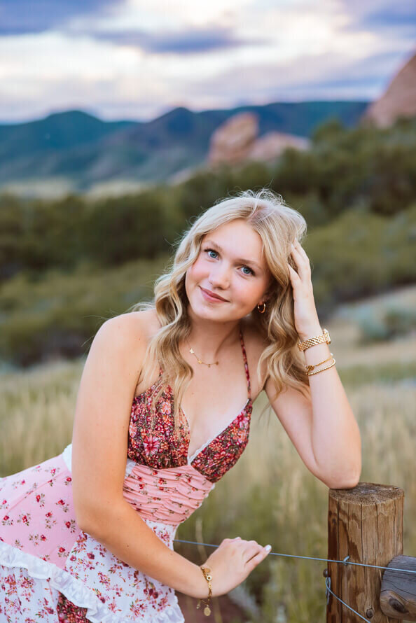 Girl leans on post with mountains behind her.