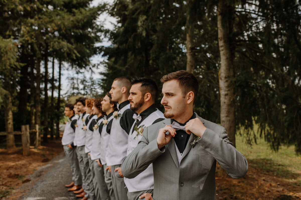 Groom tightening bow tie in front of line of groomsmen