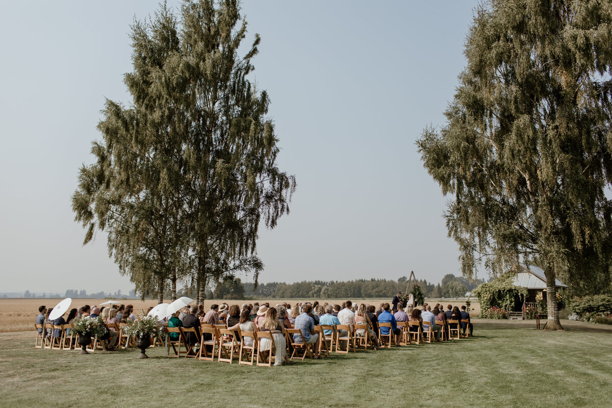 A beautiful landscape of an outdoor summer wedding ceremony at The Saltbox Barn on Fir Island in the PNW. Captured by Fort Worth Wedding Photographer, Megan Christine Studio