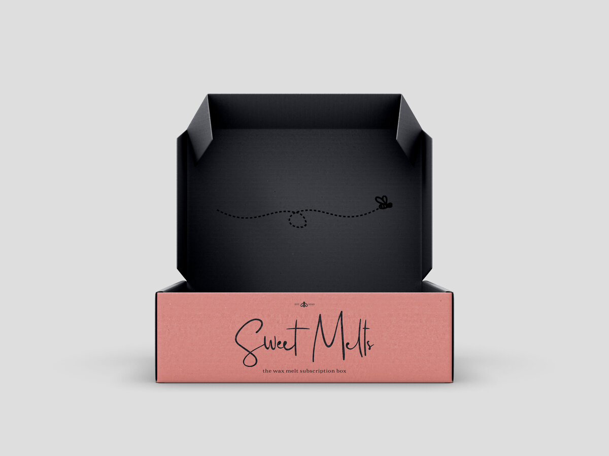 Packaging for a wax melt subscription box. The outside of the box is pink with the logo on the front. The box is open revealing a black interior with a image of a bee flying on the inside of the box.