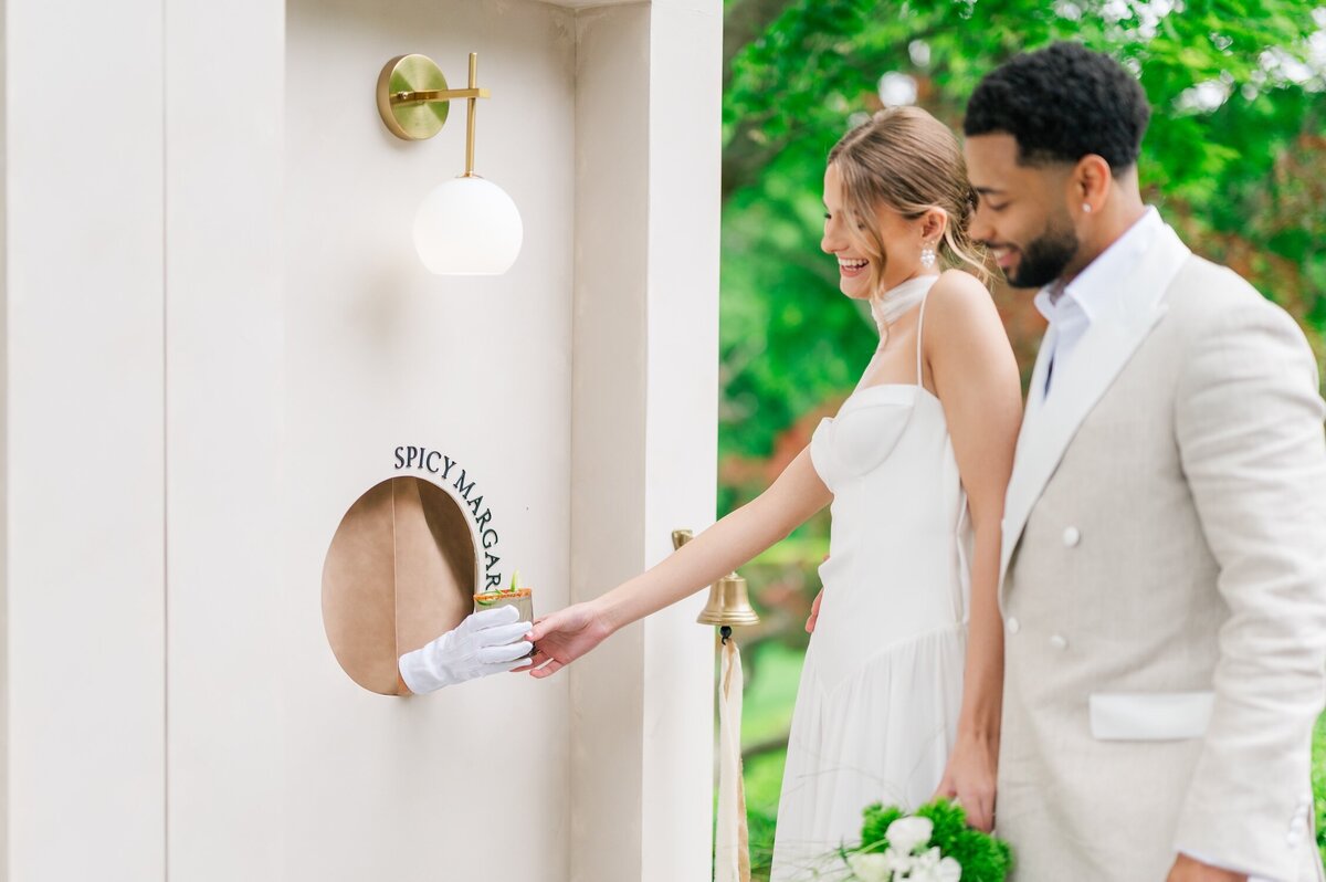 A bride and groom laugh as they grab a drink from an interactive seating chart outside of Glen Manor House. 
