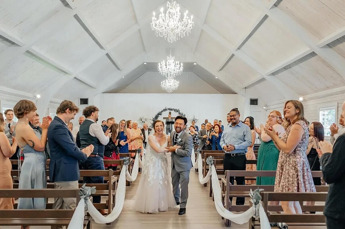 couple smiling that just got married walking down the isle with people cheering. At pinecrest event center in Colorado