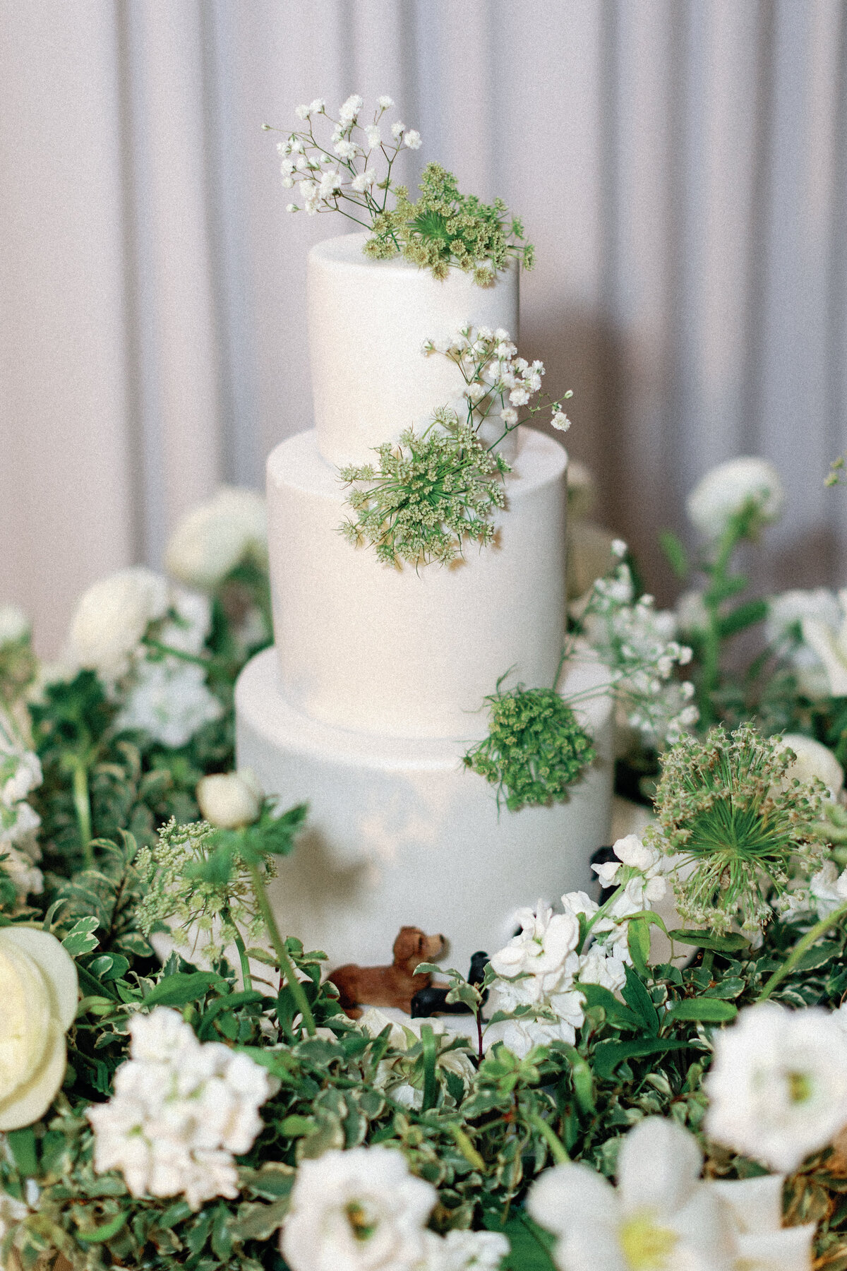 four tier wedding cake in white and green floral meadow with puppy figurines 